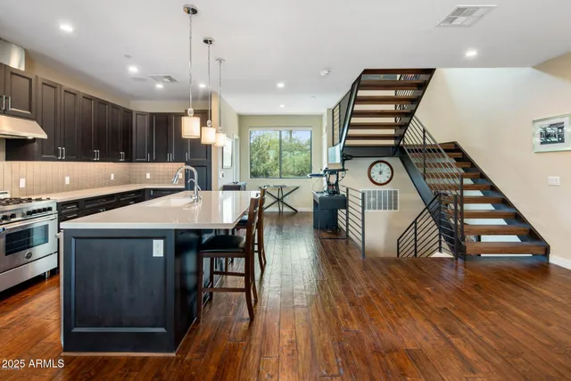 a kitchen with stainless steel appliances granite countertop a stove top oven a refrigerator a dining table and chairs with wooden floor