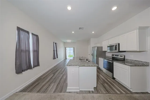 a large white kitchen with stainless steel appliances granite countertop a stove a sink a refrigerator and white cabinets with wooden floor