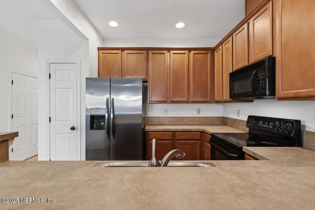 a kitchen with granite countertop a refrigerator a sink a stove a microwave and wooden cabinets