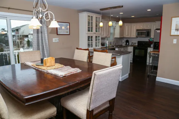 a living room with stainless steel appliances kitchen island granite countertop a stove a refrigerator a kitchen island a dining table and chairs with wooden floor