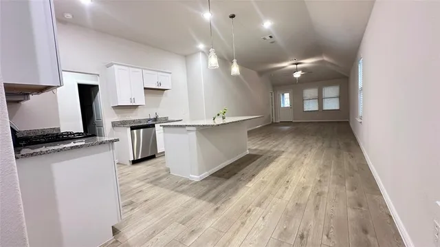 an empty room with wooden floor a ceiling fan and kitchen view