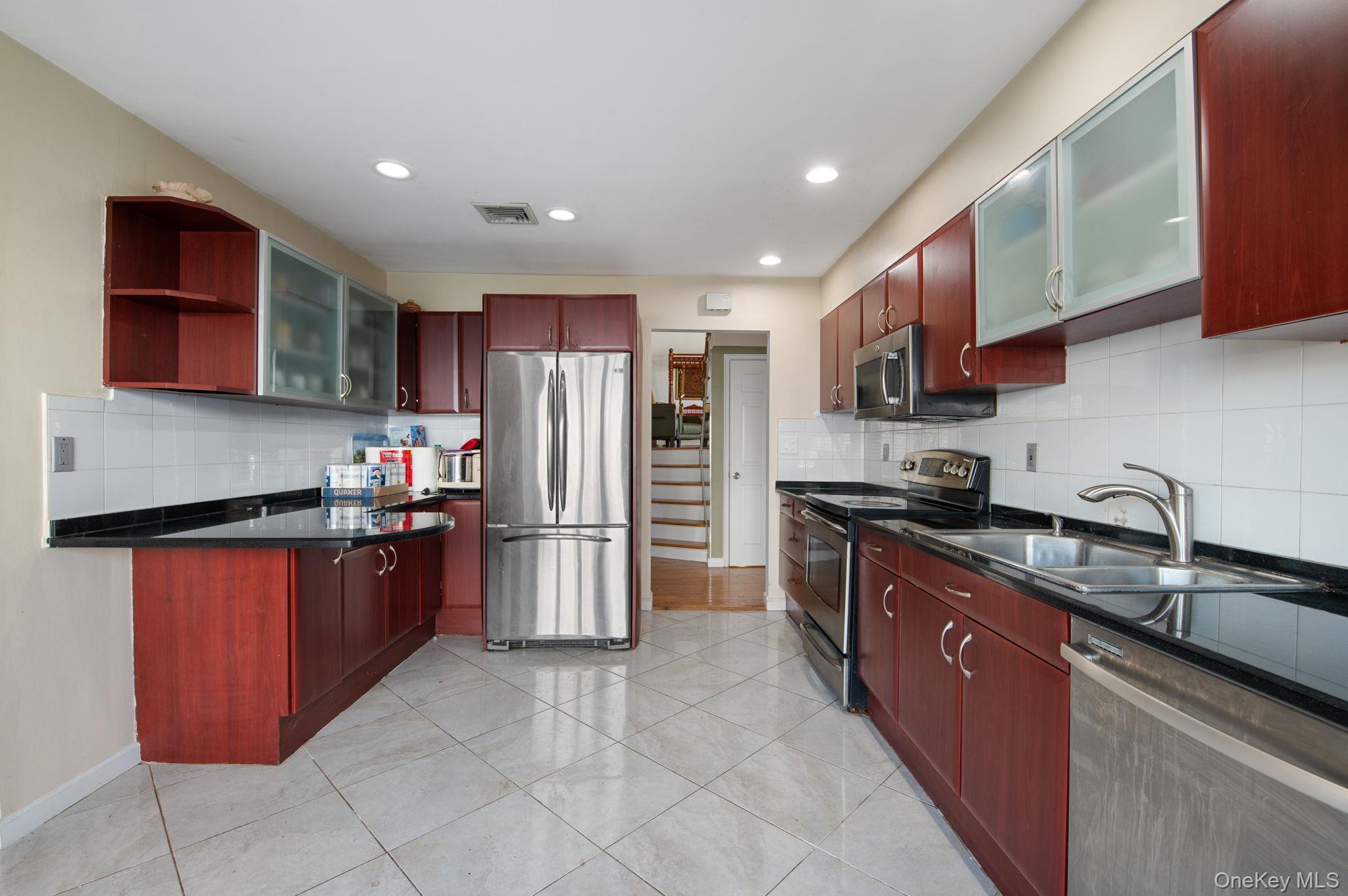 89 Nottingham Road Manhasset Hills, NY 11040 - Photo 9 of 39 Kitchen featuring glass insert cabinets, dark brown cabinets, appliances with stainless steel finishes, open shelves, and tasteful backsplash