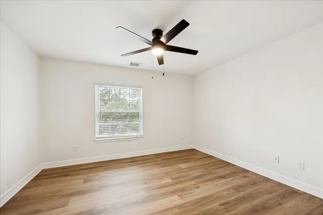a view of empty room with wooden floor and fan