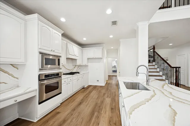 a kitchen with stainless steel appliances kitchen island granite countertop a stove a sink a refrigerator and white cabinets with wooden floor