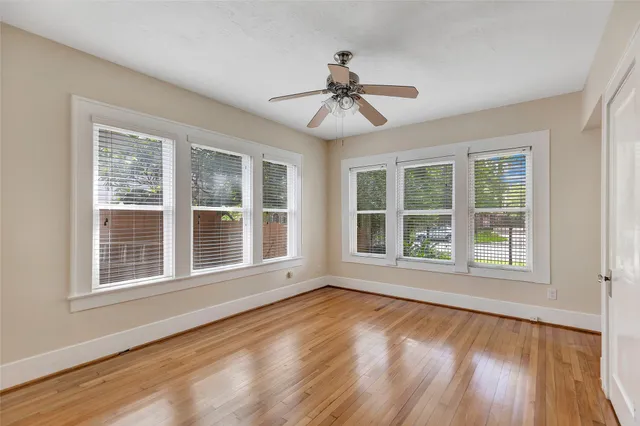 an empty room with wooden floor fan and windows