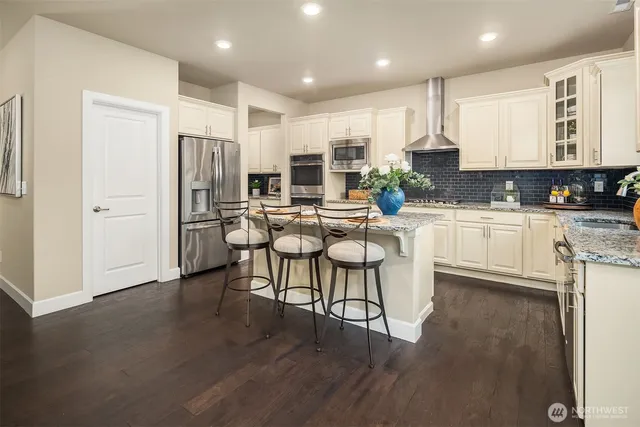 a kitchen with stainless steel appliances granite countertop a refrigerator a sink dishwasher a stove and a microwave oven with wooden floor