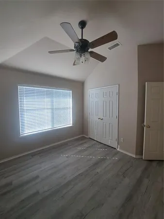 an empty room with wooden floor ceiling fan and windows