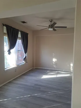 an empty room with wooden floor ceiling fan and windows
