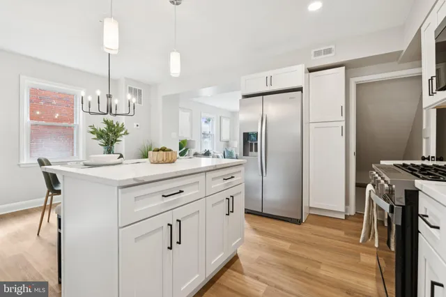 a kitchen with stainless steel appliances kitchen island granite countertop a refrigerator a sink dishwasher a dining table and chairs with wooden floor