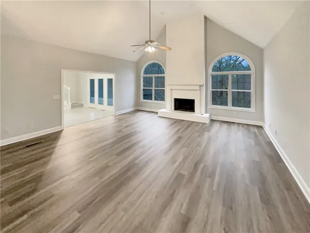 an empty room with wooden floor fireplace and windows