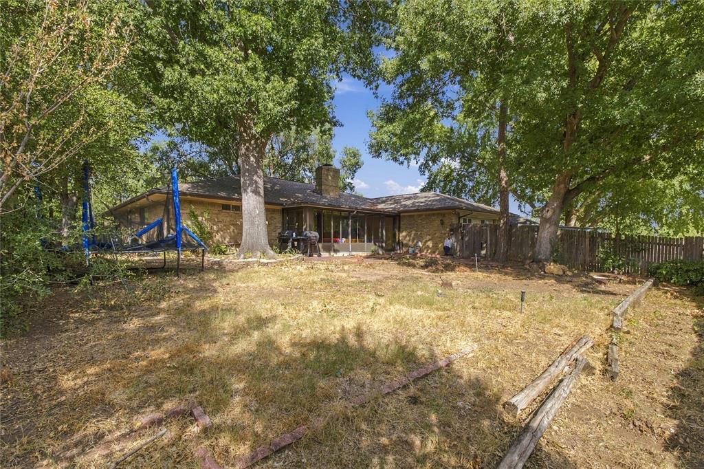 1320 Cheyenne Road Lewisville, TX 75077 - Photo 24 of 27 Expansive backyard featuring mature trees, a wood privacy fence, and an exterior brick finish