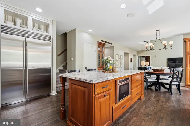 a kitchen with stainless steel appliances granite countertop a kitchen island a stove a refrigerator a dining table and chairs with wooden floor