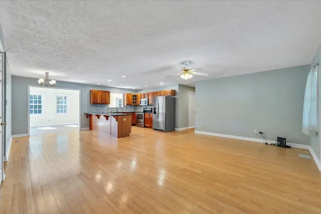 a large kitchen with stainless steel appliances granite countertop a refrigerator a sink dishwasher a oven and a dining table with wooden floor