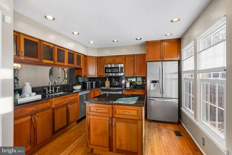 a kitchen with stainless steel appliances granite countertop a refrigerator a oven a sink with wooden cabinets and wooden floor