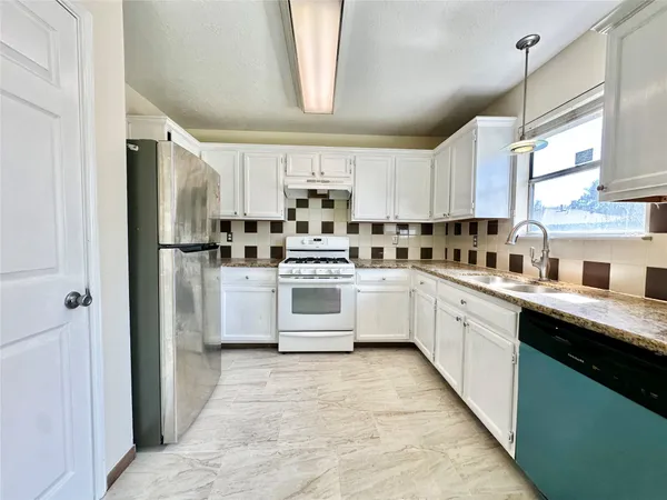 a white kitchen with stainless steel appliances granite countertop a stove a sink dishwasher and a refrigerator