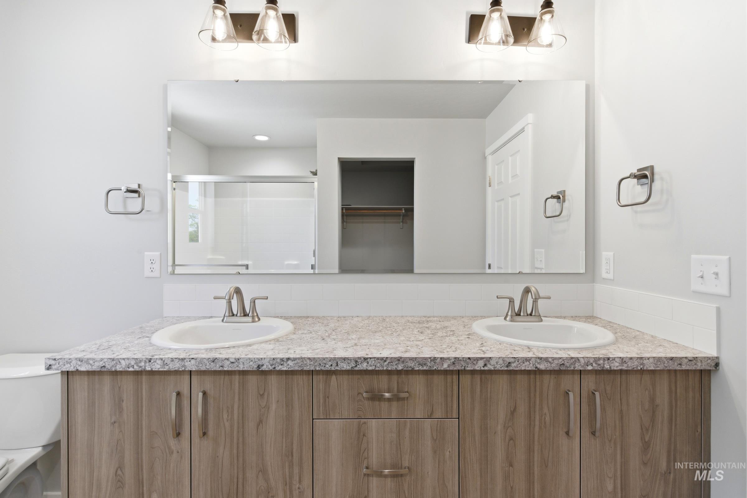 2374 West Fallon Loop Nampa, ID 83651 - Photo 23 of 24 Double vanity featuring wood-finish cabinetry, stone-look countertops, integrated sinks, and brushed nickel hardware