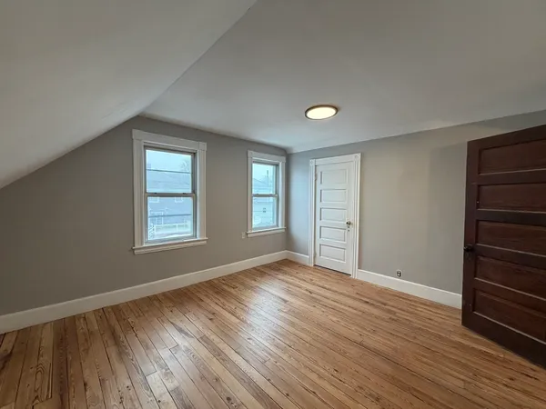 an empty room with wooden floor closet and windows