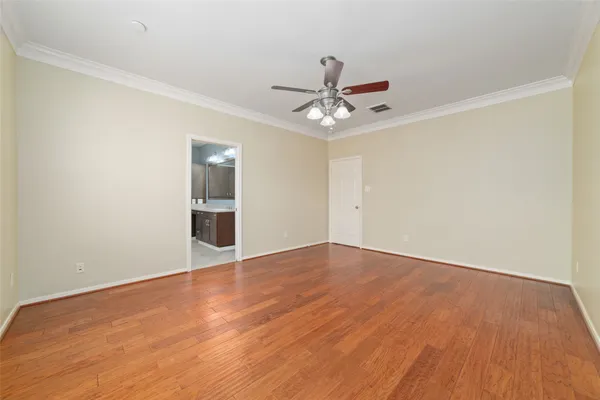 a view of an empty room with wooden floor and a ceiling fan
