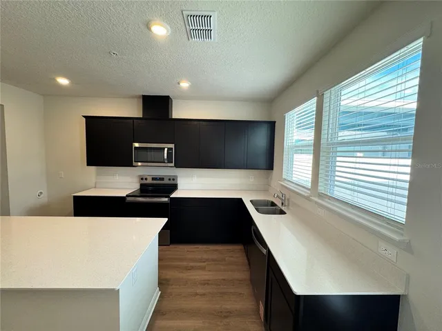 a kitchen with stainless steel appliances a sink a stove a refrigerator cabinets and wooden floor