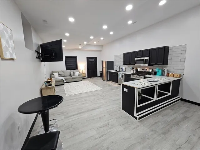 a living room with stainless steel appliances furniture a flat screen tv and a view of kitchen
