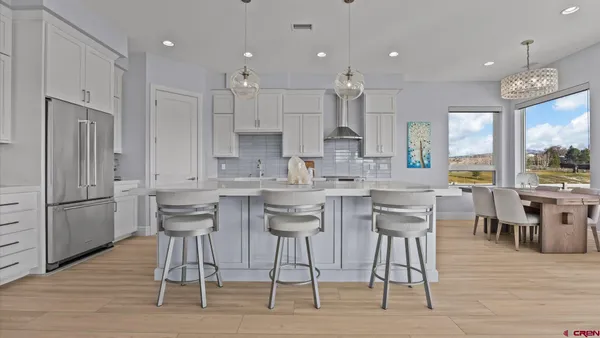 a kitchen with stainless steel appliances kitchen island granite countertop a dining table chairs and a refrigerator