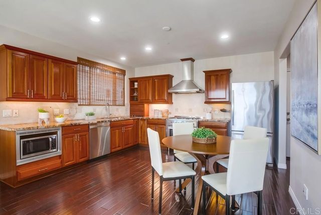 a kitchen with stainless steel appliances kitchen island granite countertop a refrigerator a stove top oven a sink dishwasher and white cabinets with wooden floor