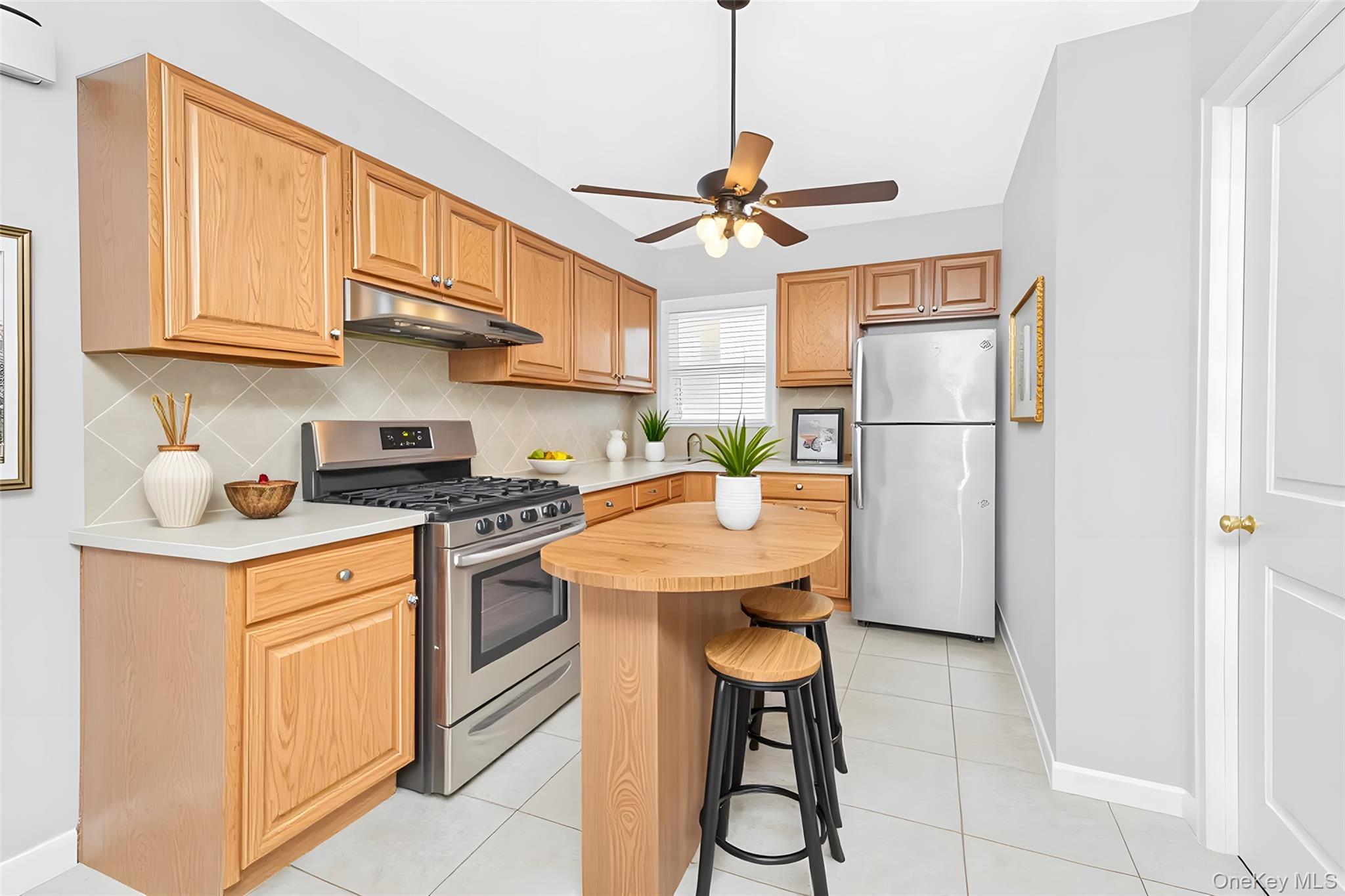1616 Library Avenue Bronx, NY 10465 - Photo 17 of 20 Kitchen featuring appliances with stainless steel finishes, backsplash, light tile patterned flooring, under cabinet range hood, and a ceiling fan