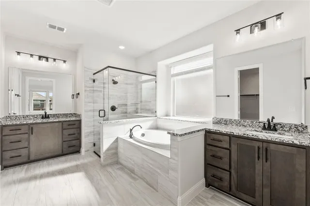 a spacious bathroom with a granite countertop double vanity sink a bathtub a mirror and shower
