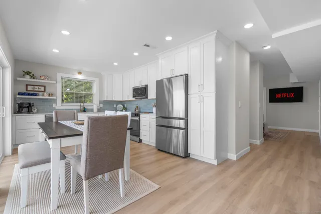 a kitchen with stainless steel appliances granite countertop a refrigerator a stove a sink dishwasher and a dining table with wooden floor