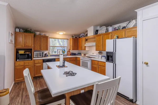 a kitchen with a refrigerator a stove a sink dishwasher a dining table and chairs with wooden floor