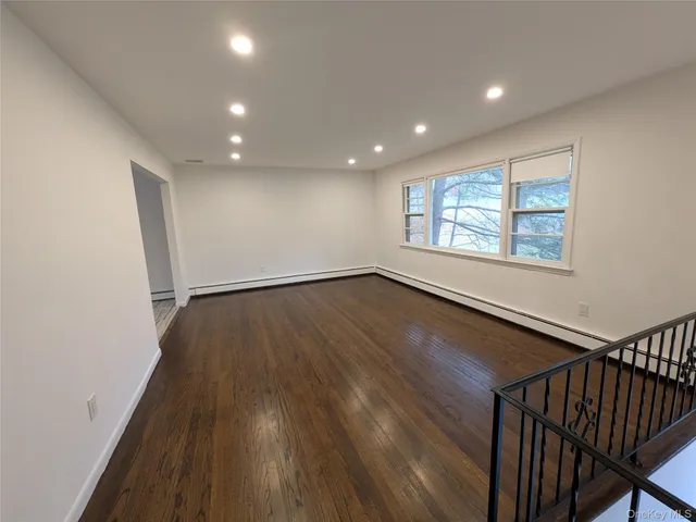 a view of an empty room with wooden floor and windows