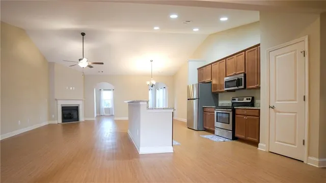 a open kitchen with stainless steel appliances granite countertop a stove top oven a refrigerator a kitchen island with cabinets and wooden floor