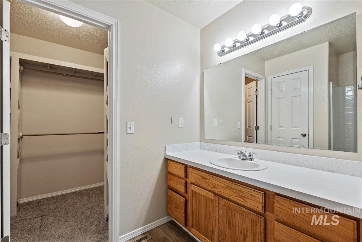 994 North Gray Cloud Way Meridian, ID 83642 - Photo 21 of 28 Full bathroom featuring a walk in closet, vanity, a textured ceiling, and dark wood-style floors