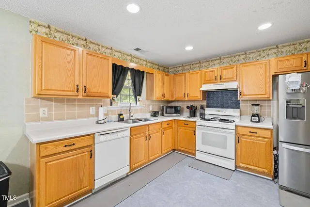 a kitchen with stainless steel appliances granite countertop a sink a stove a refrigerator cabinets and a window
