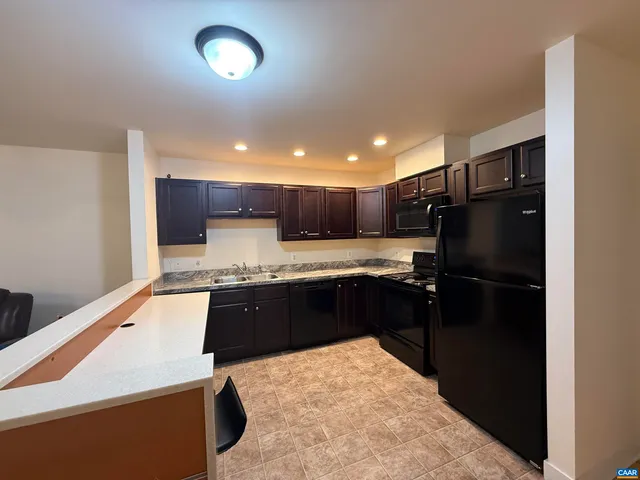 a kitchen with stainless steel appliances kitchen island granite countertop a refrigerator a sink a stove and black cabinets