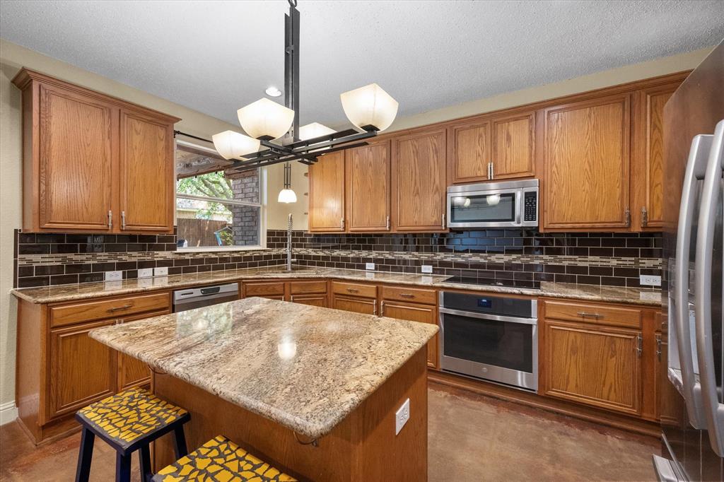 1305 Liverpool Lane Mansfield, TX 76063 - Photo 22 of 40 Well-appointed kitchen featuring wood cabinetry, granite countertops, a dark tile backsplash, and stainless steel appliances, including an oven, microwave, and refrigerator