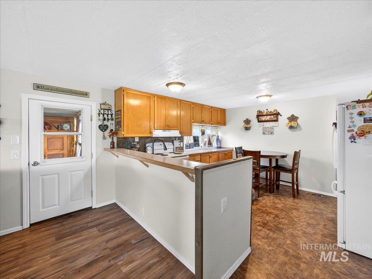 9228 Washoe Road Payette, ID 83661 - Photo 19 of 49 Kitchen featuring a peninsula, white appliances, wood finish cabinetry, a textured ceiling, and a breakfast bar area
