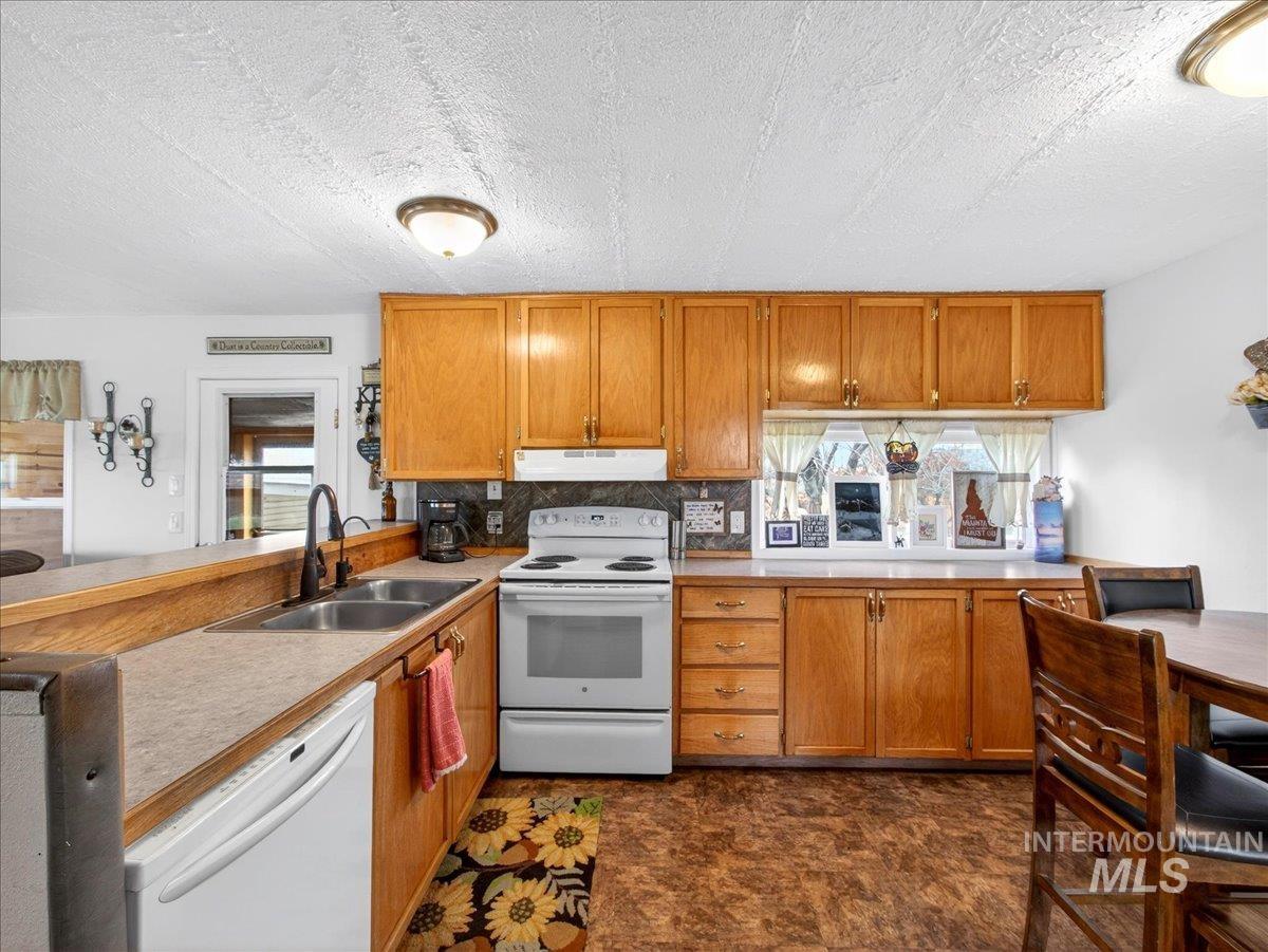 9228 Washoe Road Payette, ID 83661 - Photo 20 of 49 Kitchen featuring a peninsula, white appliances, wood finish cabinets, light countertops, and tasteful backsplash