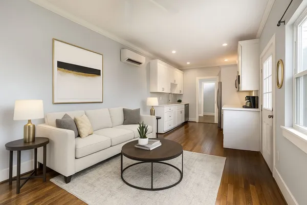 a living room with white couches and kitchen view with wooden floor