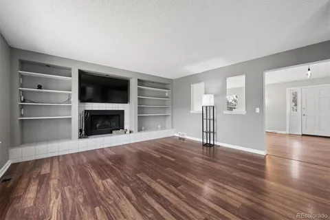a view of an empty room with wooden floor and a fireplace