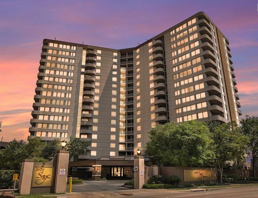 This photo shows a modern high-rise residential building with multiple floors, featuring a sleek design and a warm, inviting exterior. Surrounded by greenery, it’s set against a beautiful sunset sky, providing an elegant urban living option.