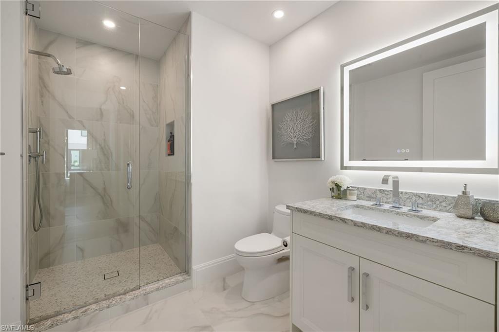 1130 3rd Avenue South, Unit 210 Naples, FL 34102 - Photo 26 of 48 a bathroom with a granite countertop sink a toilet a mirror and shower