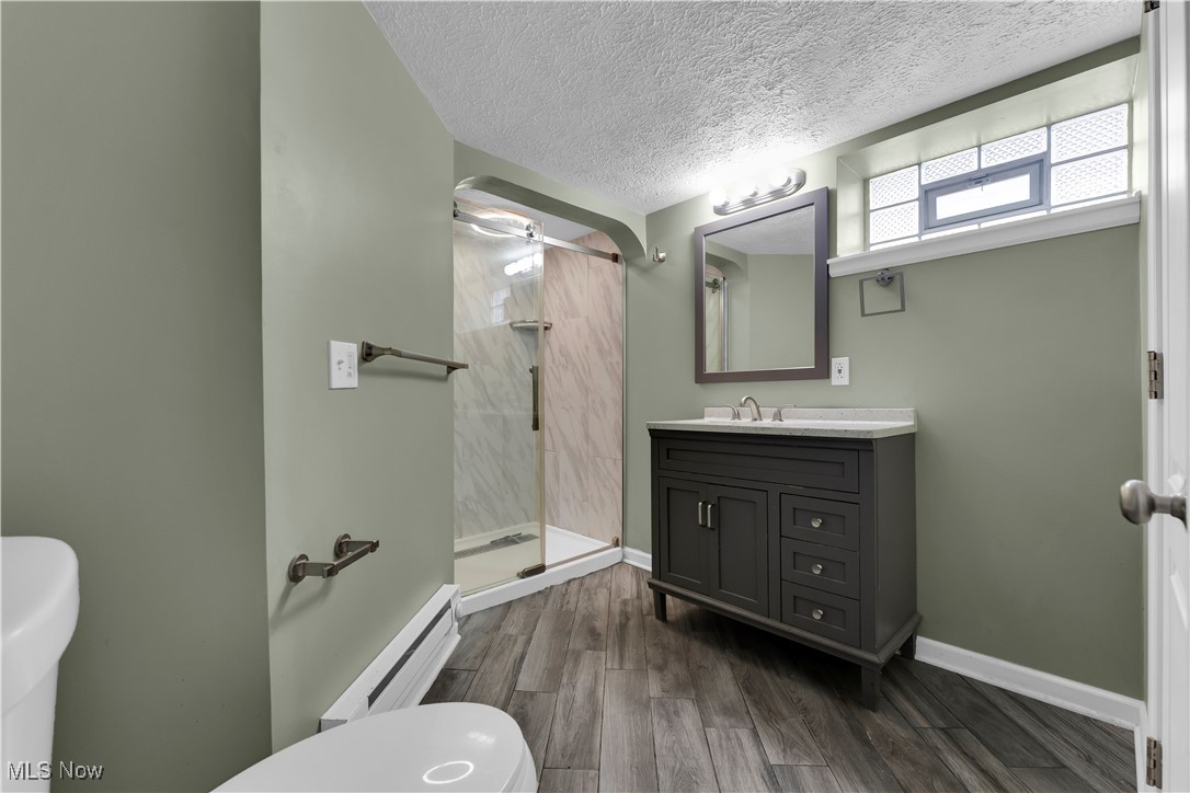 3739 Warren Road Cleveland, OH 44111 - Photo 8 of 40 Bathroom with dark wood-style floors, a shower stall, baseboard heating, vanity, and a textured ceiling
