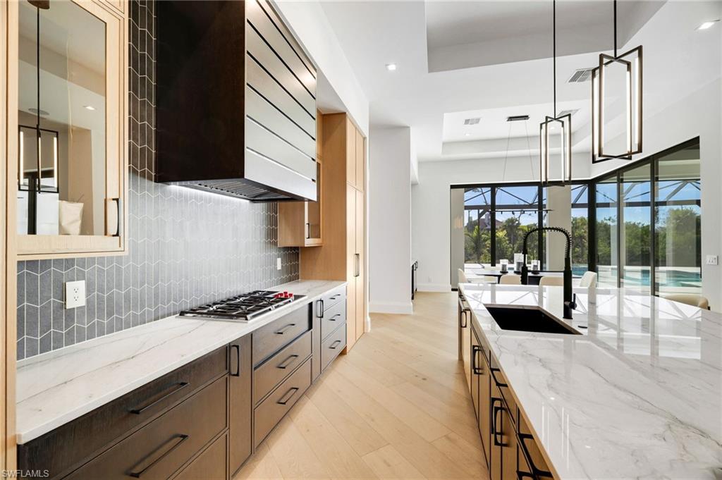 15850 Hampton View Fort Myers, FL 33908 - Photo 5 of 38 Two tone kitchen featuring light stone countertops, decorative light fixtures, a tray ceiling, light wood-style flooring, and decorative backsplash