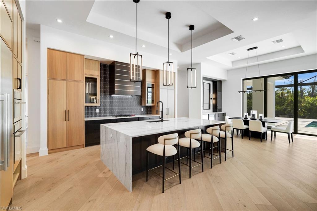 15850 Hampton View Fort Myers, FL 33908 - Photo 7 of 38 Kitchen featuring modern cabinets, a raised ceiling, hanging light fixtures, light stone counters, and light wood-type flooring