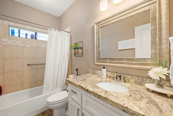 a bathroom with a granite countertop sink a toilet a mirror and bathtub