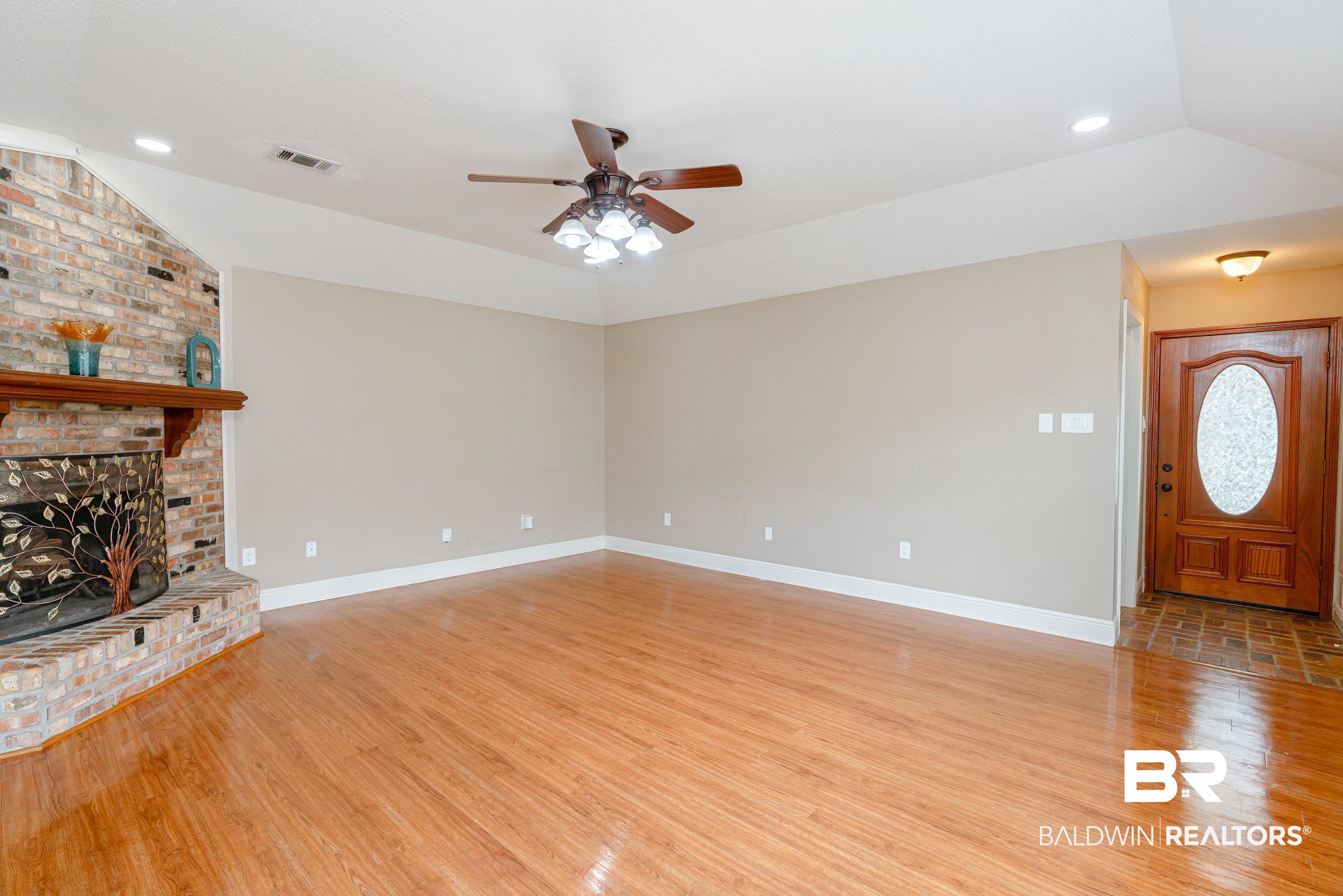 23 Old Mill Court Mobile, AL 36608 - Photo 12 of 37 Unfurnished living room with light wood-type flooring, ceiling fan, brick wall, a fireplace, and vaulted ceiling