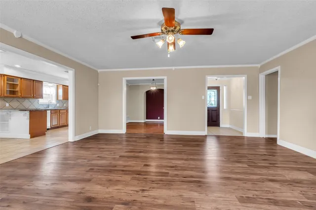 a view of an empty room with wooden floor and a kitchen