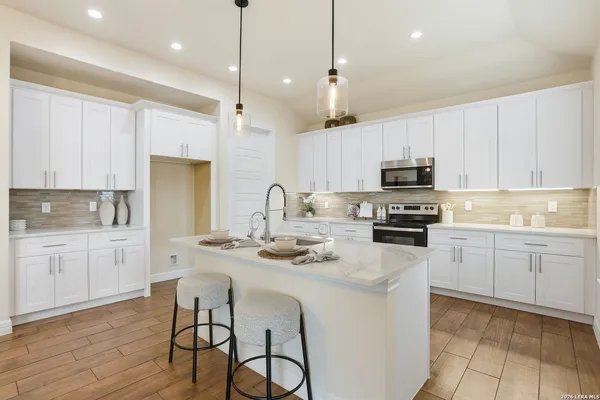 a kitchen with kitchen island granite countertop a sink stove and white cabinets with wooden floor