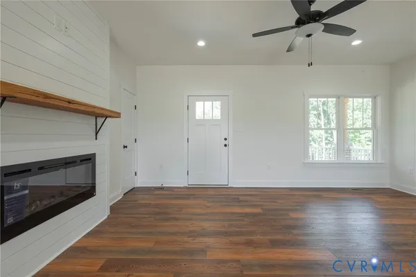 an empty room with wooden floor a ceiling fan a fireplace and windows